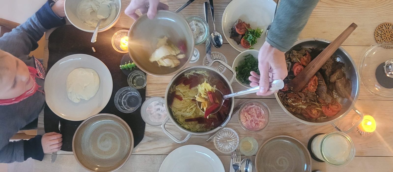 Vater schöpft seinem Kind Fleischbrühe an einem gedeckten Tisch mit Leber, Sauerkraut und weiteren traditionellen Lebensmitteln